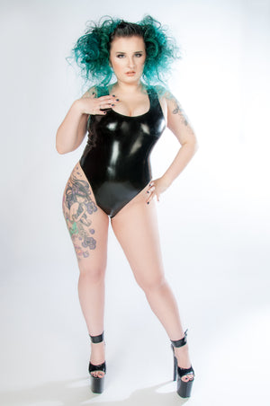 Woman with green hair stands in high heels and black latex bodysuit.